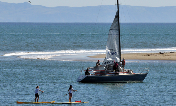 The harbor mouth was a hub of activity on Sunday as Stand-Up Paddleboarders watch a sailboat take down its sail upon re-entering the harbor