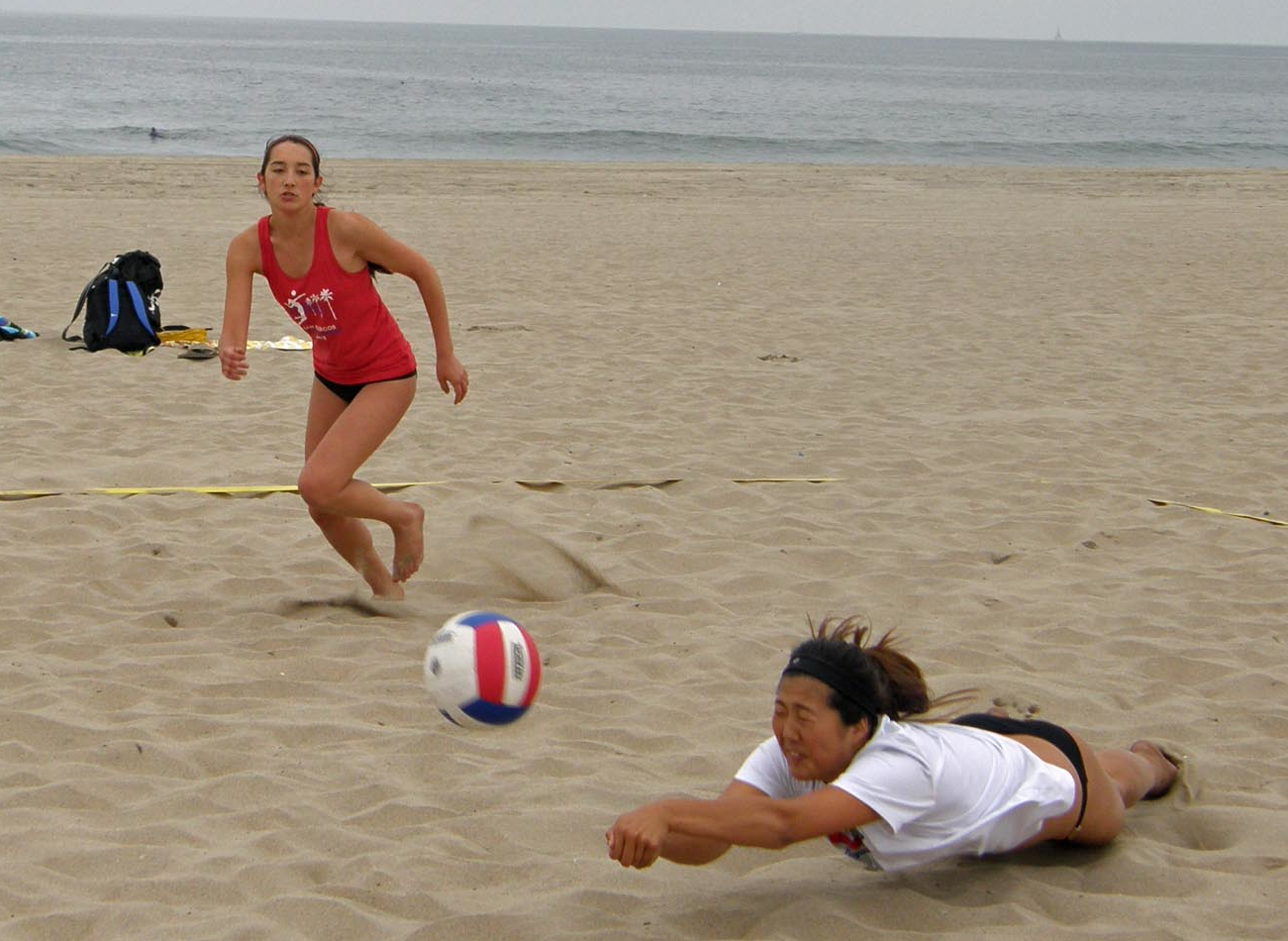 Katie Kim of San Marcos dives for a ball as teammate Andie  O'Donnell rushes in to help during Interscholastic Beach Volleyball League action in Playa del Rey.