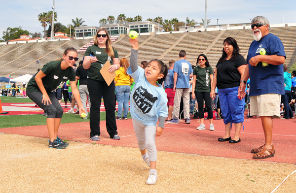 Community volunteers watch an enthusiastic young thrower compete in the ball throw at the School Games at Santa Barbara City College.